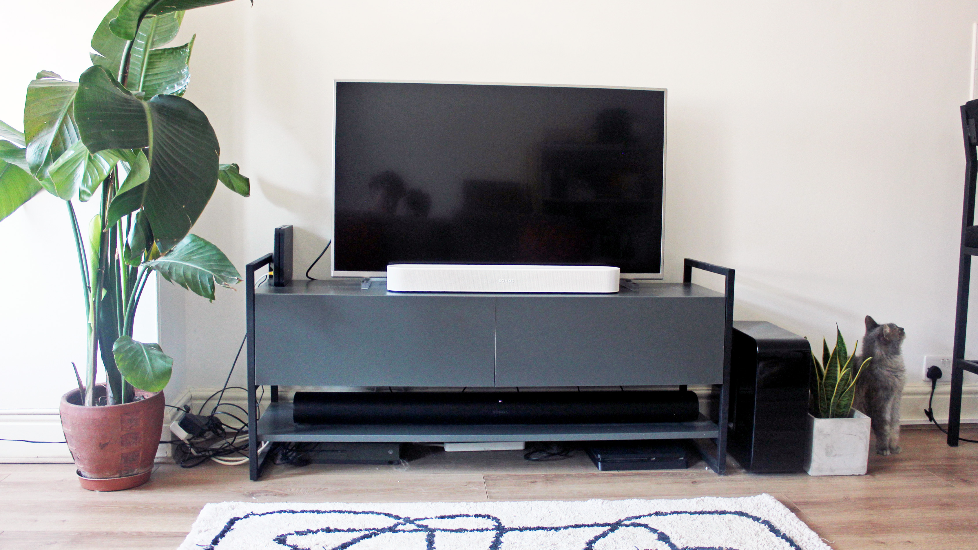 the sonos beam gen 2 soundbar in white in a living room on a tv cabinet underneath a tv display